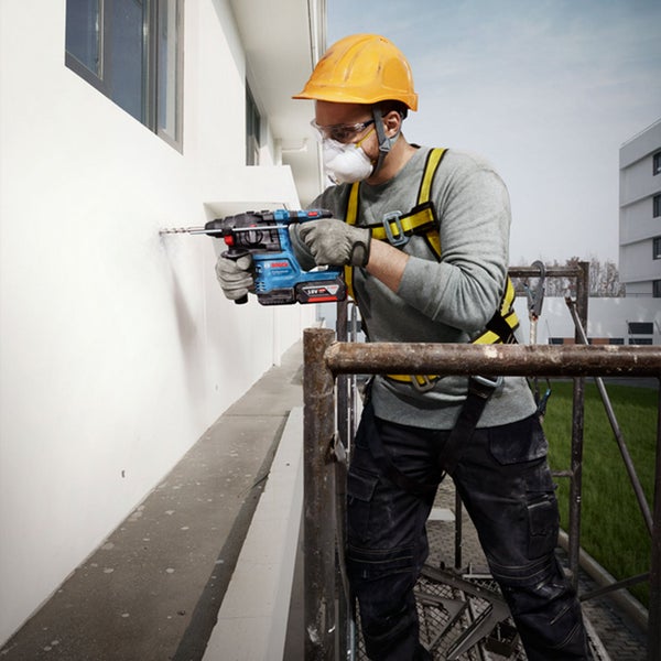 Handwerker mit Bosch Akku Bohrhammer bei der Arbeit auf einem Gerüst an einer Hauswand im Außenbereich.