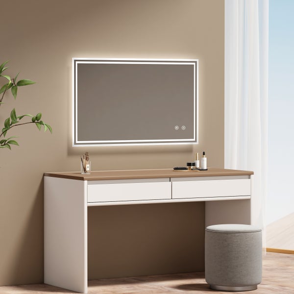 Rechteckiger Badezimmerspiegel mit LED Beleuchtung und Touch Funktion über einem modernen Schminktisch mit zwei Schubladen und gepolstertem Hocker.