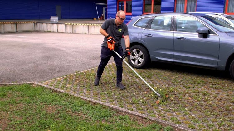 Mann entfernt Unkraut mit einem Unkrautentferner auf einer gepflasterten Fläche.