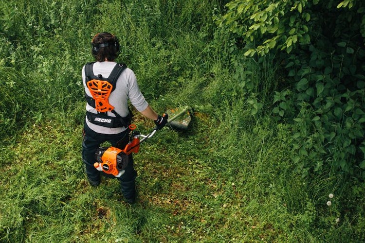 Eine Person benutzt einen Rasentrimmer im Garten mit Echo Logo.