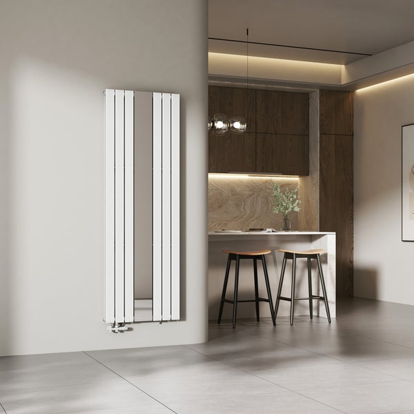 Moderner vertikaler Designheizkörper mit integriertem Spiegel an einer Wand in einer hellen Küche mit Barhockern und Holzschränken.