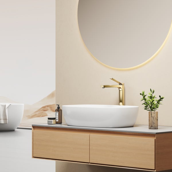 Modernes Badezimmer mit Waschtisch aus Holz, Aufsatzwaschbecken und goldener Waschtischarmatur vor einem runden beleuchteten Spiegel.