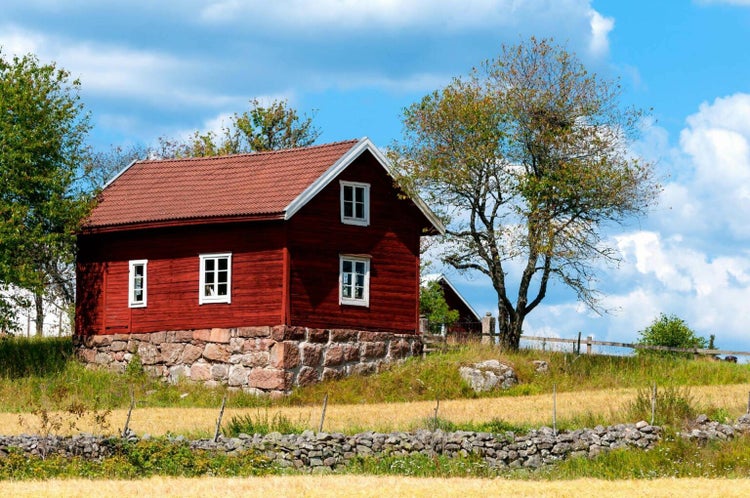 Klassisches rotes Holzhaus im skandinavischen Stil mit weißen Fensterrahmen und Natursteinsockel in einer ländlichen Gartenlandschaft.