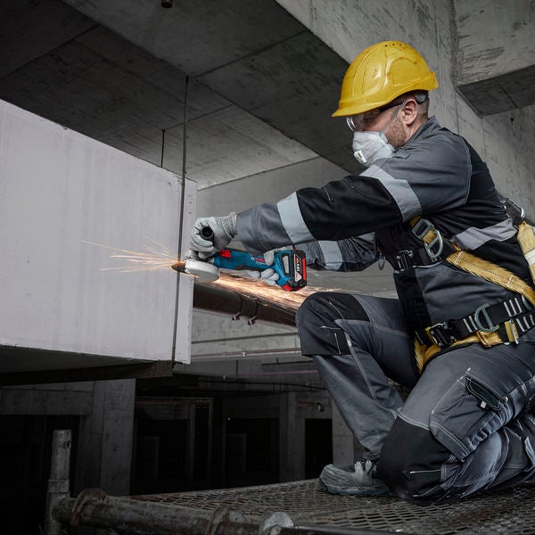 Ein Arbeiter benutzt einen Akku-Winkelschleifer auf einer Baustelle, Funken fliegen.