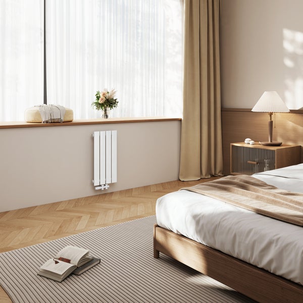 Ein moderner, vertikaler Flachheizkörper unter einem Fenster in einem elegant eingerichteten Schlafzimmer mit Holzparkett und Tageslicht.