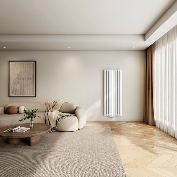 Ein moderner Wohnbereich mit hellem Sofa, Holztisch, Fischgrätparkett und einem vertikalen Designheizkörper an der Wand.