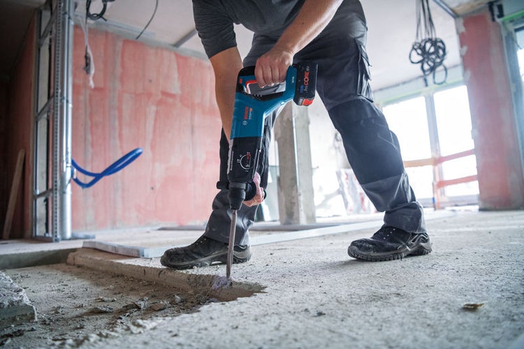 Handwerker arbeitet mit einem Bohrhammer auf einer Baustelle, um einen Schlitz in einen Betonboden zu stemmen.