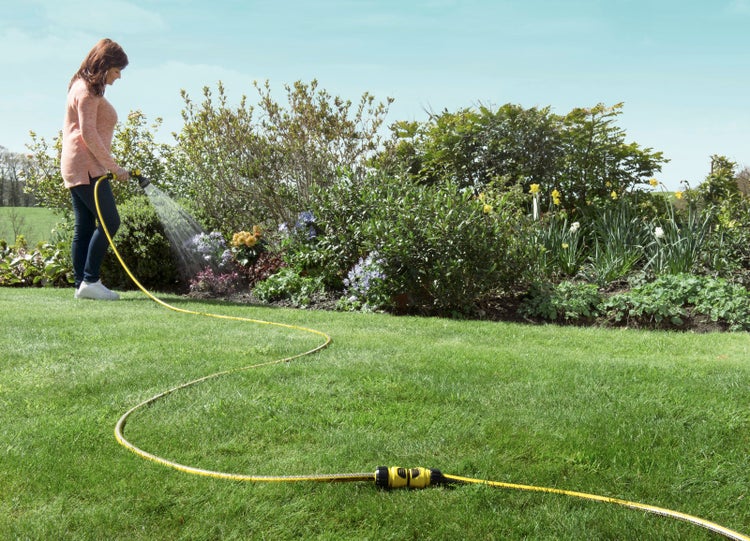 Eine Frau bewässert mit einem Gartenschlauch einen Garten