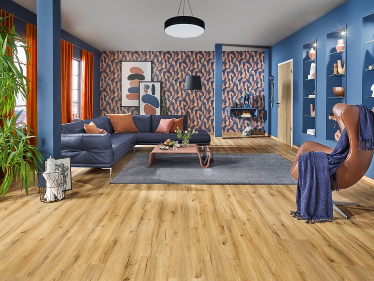 Modernes Wohnzimmer mit blauen Wänden, gemusterter Tapete, hellem Boden in Eichenoptik, blauem Ecksofa und braunem Ledersessel.