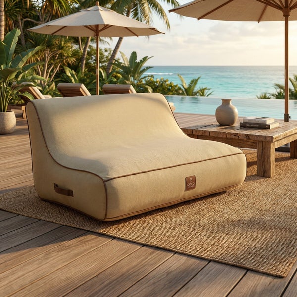 Beiges Outdoor-Sitzkissen auf einer Holzterrasse mit Jute-Teppich, Pool und Meerblick im Hintergrund, Coco Lounge Logo.