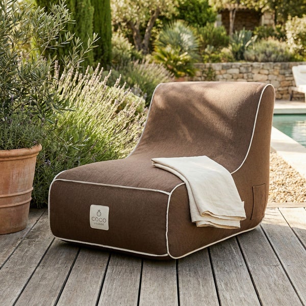 Brauner Outdoor-Sitzsack Coco Lounge mit weißem Saum auf einer Holzterrasse am Pool in einem hellen Garten.