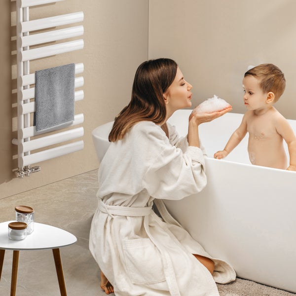 Helle, freundliche Badezene mit einem Handtuchwärmer, einer Mutter und einem Kind in der Badewanne.