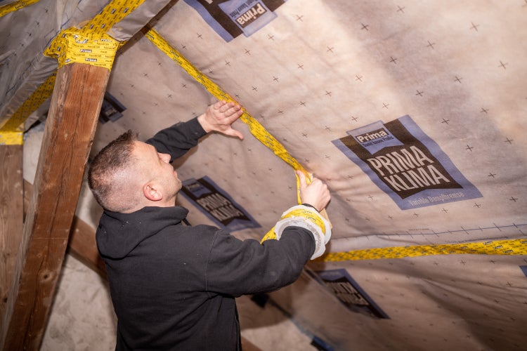 Handwerker bei der Montage einer Prima Klima Dampfbremse an der Dachschräge, Verklebung der Überlappungen mit Systemklebeband.