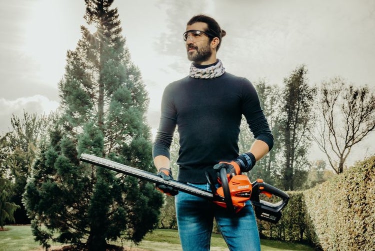 Mann mit Schutzbrille hält eine Heckenschere im Garten.