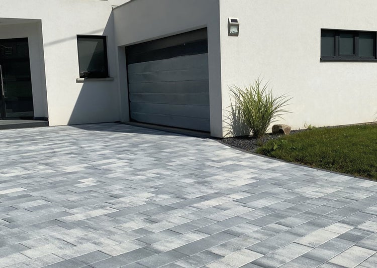 Hauseinfahrt mit grau-weiß nuanciertem Pflasterstein vor einer modernen weißen Fassade und Garage.