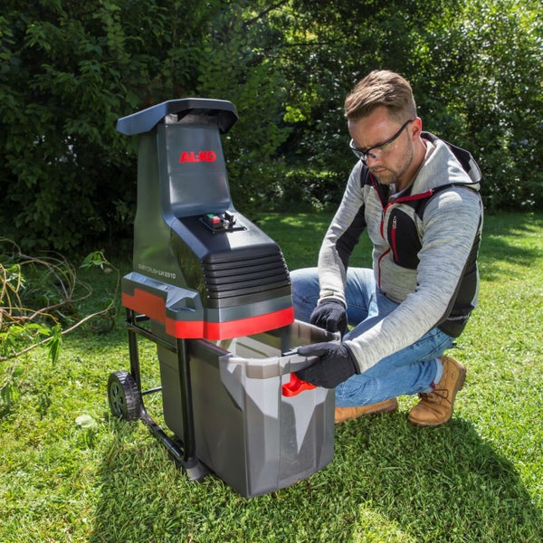 Ein Mann mit Schutzbrille und Handschuhen setzt den Auffangbehälter in einen AL-KO Gartenhäcksler auf einem Rasen ein.