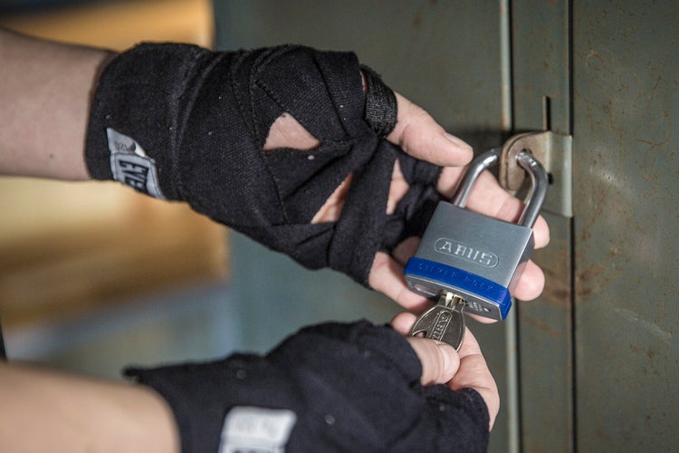 Hände in Bandagen öffnen ein ABUS Vorhängeschloss an einem Metallspind mit einem Schlüssel.