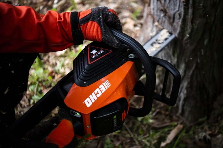 Eine Person bedient eine Akku-Kettensäge der Marke Echo beim Sägen eines Baumes.