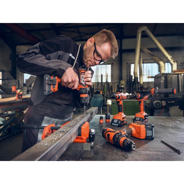 Handwerker bohrt mit einem Akkubohrschrauber in ein Metallprofil an einer Werkbank in einer professionellen Werkstatt mit weiteren Elektrowerkzeugen.