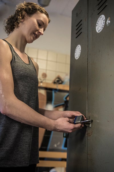 Eine Frau sichert einen Metallspind in einer Umkleidekabine mit einem Vorhängeschloss.