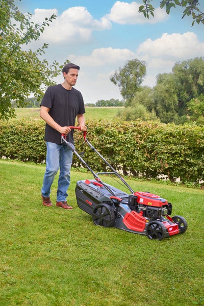 Ein Mann mäht mit einem AL-KO Benzinrasenmäher eine Grünfläche in einem Garten.