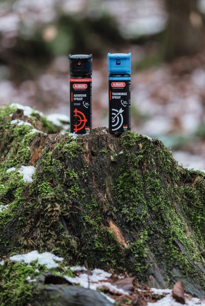 ABUS Abwehrspray und Trainingsspray auf einem moosbewachsenen Baumstumpf in einem verschneiten Wald.