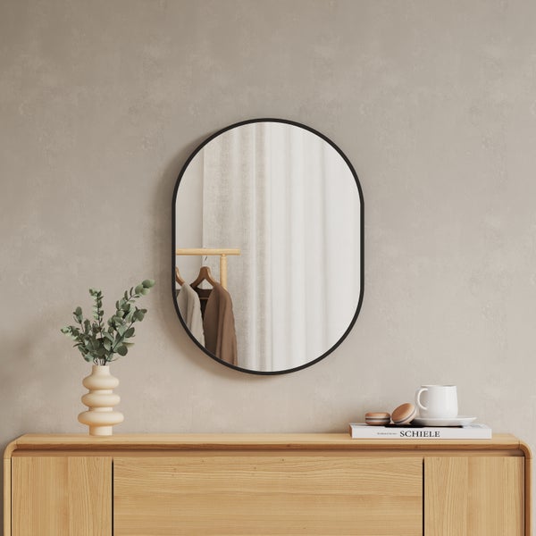 Ovaler Wandspiegel mit schwarzem Rahmen über einem Sideboard aus Holz in einem hellen, minimalistisch eingerichteten Raum.