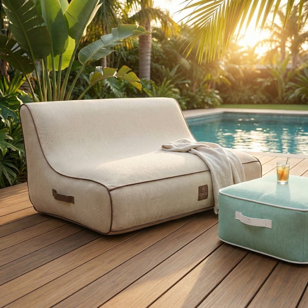 Modernes Outdoor-Loungesofa aus beigefarbenem Stoff mit brauner Paspelierung und passendem türkisfarbenem Hocker auf einer Holzterrasse am Pool.