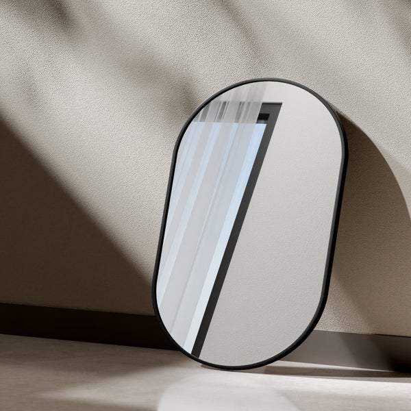 Ovaler Wandspiegel mit schmalem schwarzem Rahmen, modernes Design, an eine Wand gelehnt.
