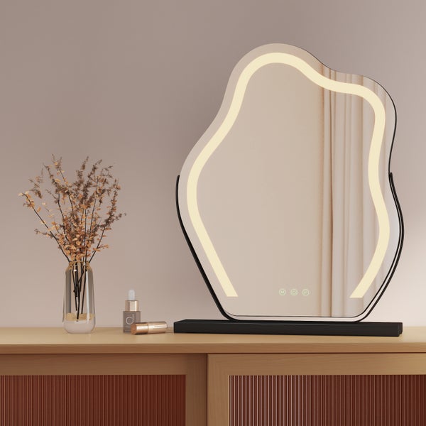 Dekorative Szene mit einem unregelmäßig geformten Spiegel mit Beleuchtung auf einem Tisch mit Dekorationen