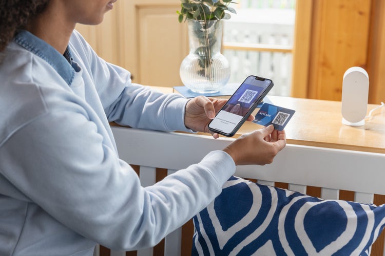 Person scannt den QR-Code einer Smart Home Keycard mit einem Smartphone. Im Hintergrund eine Smart Home Zentrale auf einem Holztisch.