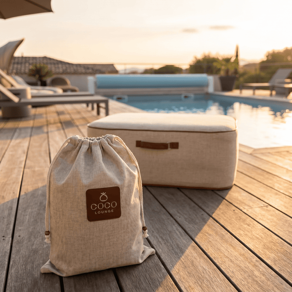 Beige Zugbeutel mit COCO LOUNGE Logo und Sitzpouf auf einer hellen Holzterrasse am Pool.