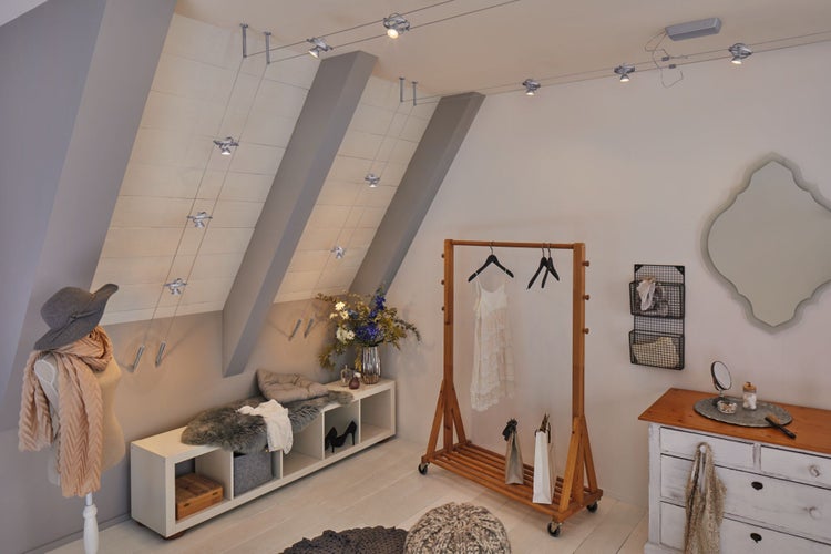 Dachgeschosszimmer mit flexibler Seilbeleuchtung, Kleiderständer, Kommode und dekorativen Elementen