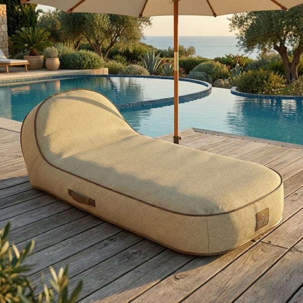 Ergonomische Outdoor-Liege in Sitzsack-Form aus beigem Gewebe auf einer Holzterrasse am Pool, moderner Stil, im Hintergrund ein Sonnenschirm.