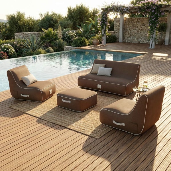 Modernes Outdoor-Lounge-Set auf einer Holzterrasse am Pool. Bestehend aus braunem Stoffsofa, zwei Sesseln und einem Hocker auf einem Jute-Teppich in heller Atmosphäre.