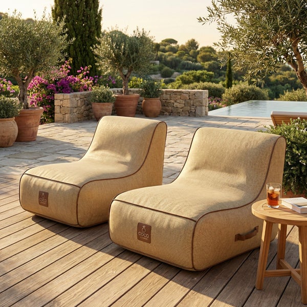Zwei beige Outdoor-Sitzsäcke aus Webstoff mit brauner Paspelierung und COCO LOUNGE Logo auf einer hellen Holzterrasse neben einem Pool.