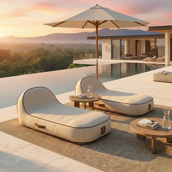 Zwei gepolsterte Outdoor-Liegen auf einer Terrasse mit Pool, Sonnenschirm und Beistelltischen aus Holz vor einer Berglandschaft.