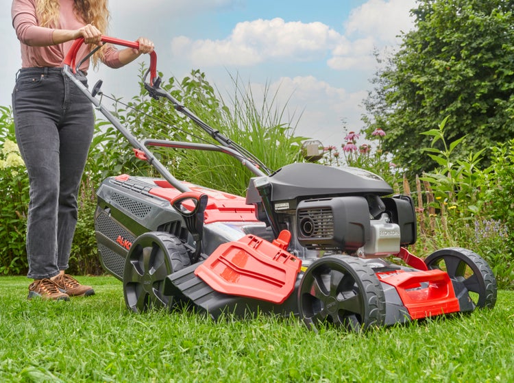 Person mäht den Rasen mit einem AL-KO Benzin-Rasenmäher mit Honda-Motor in einem Garten.