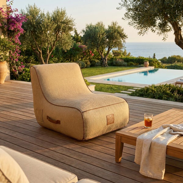 Outdoor-Loungesessel aus robustem Textilgewebe auf einer Holzterrasse in einem Garten mit Pool und Meerblick.