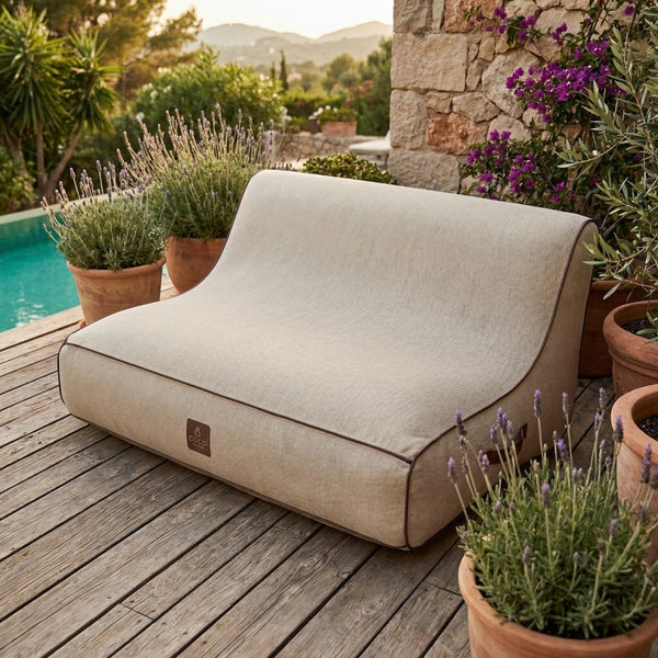 Modernes Outdoor Lounge-Sitzkissen in Beige auf einer Holzterrasse am Pool, umgeben von Lavendelpflanzen und einer Natursteinwand.