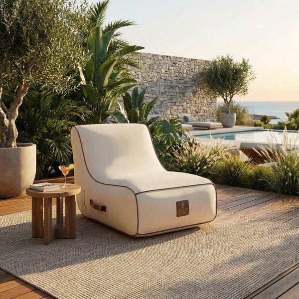 Moderner COCO LOUNGE Outdoor-Sitzsack in Beige auf einer Holzterrasse an einem Pool, umgeben von Pflanzen und einem kleinen Holztisch.