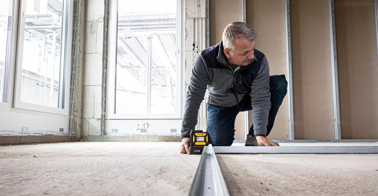 Ein Mann arbeitet mit einer Nivelliermaschine auf einem Bauprojekt, um Metallprofile auszurichten.