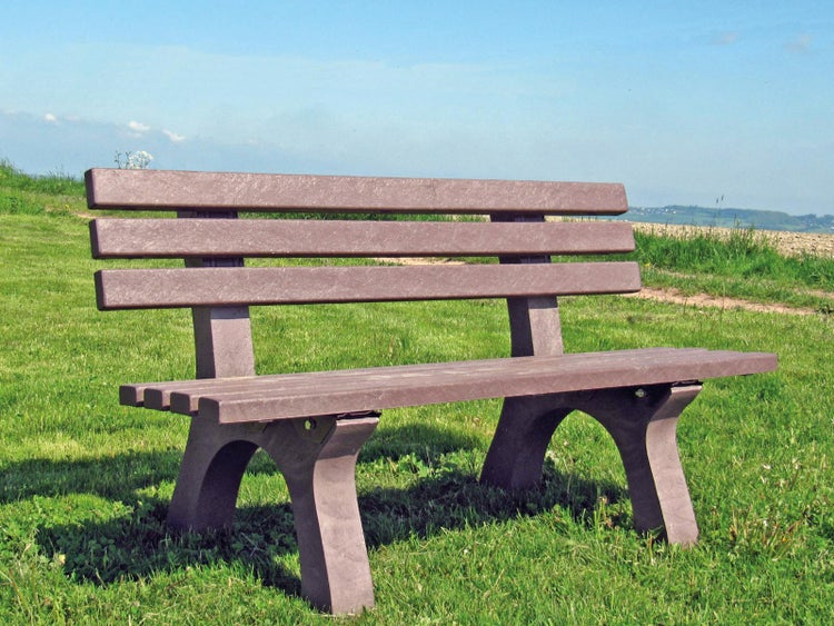Eine Gartenbank aus Kunststoff in einer Wiesenlandschaft unter blauem Himmel.