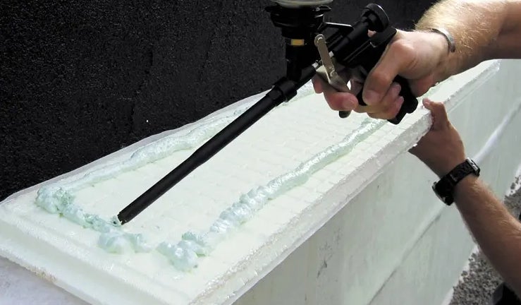 Mann trägt Bauschaum auf Dämmplatte mit Pistole auf