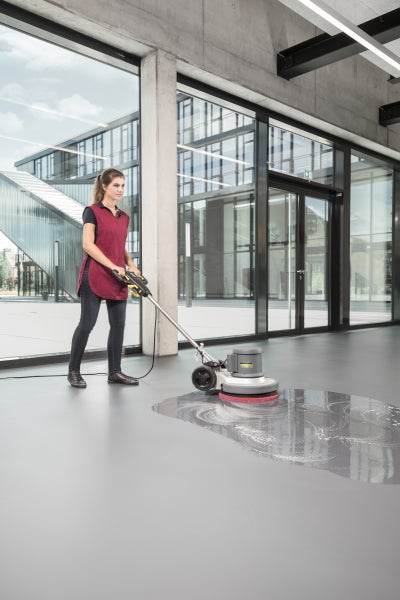 Eine Person reinigt einen glatten Boden in einem modernen Gebäude mit einer Karcher Professional Einscheibenmaschine.