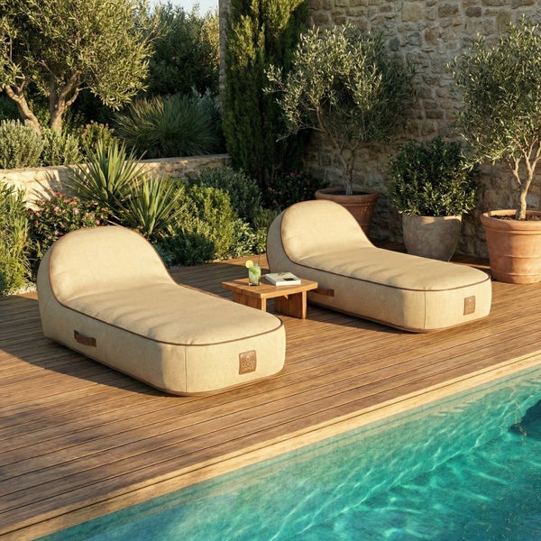 Moderne Outdoor-Liegesäcke auf einer Holzterrasse am Pool mit kleinem Beistelltisch, mediterranen Pflanzen und Steinwand im hellen Außenbereich.