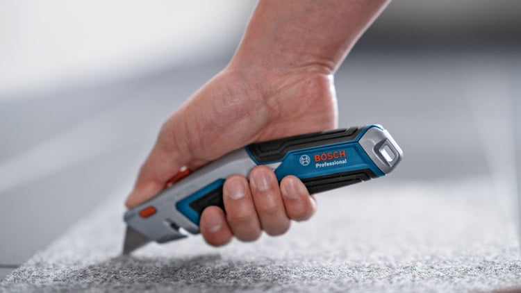 Hand schneidet Teppich mit Bosch Teppichmesser