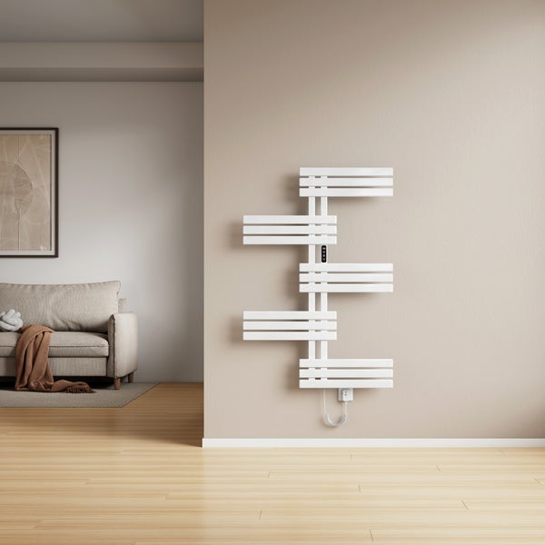 Moderner elektrischer Badheizkörper mit asymmetrischen Stufen an einer Wohnzimmerwand neben einem Sofa.