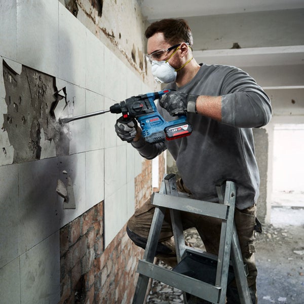 Handwerker mit Schutzausrüstung nutzt Bosch Professional Akku Bohrhammer für Abbrucharbeiten an einer Fliesenwand auf einer Leiter.