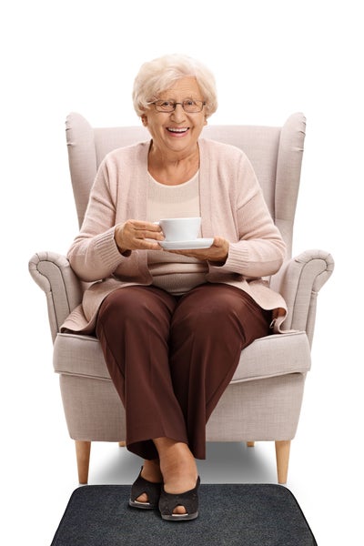 Ältere Frau sitzt in einem Sessel und hält eine Tasse mit Untertasse